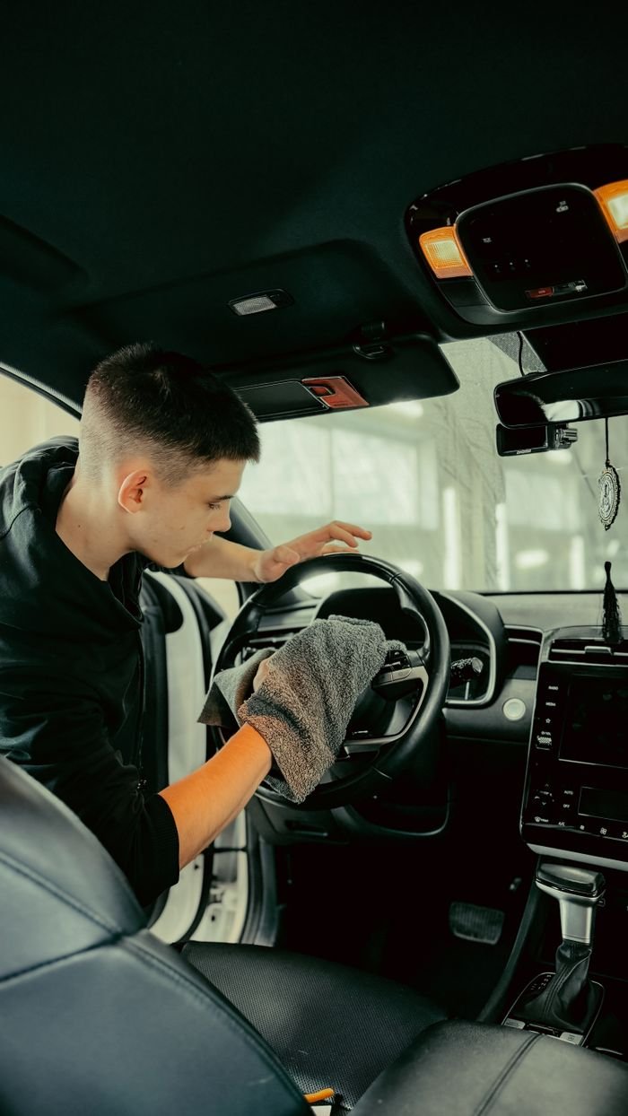 our-story-02 Young man polishing car steering wheel with cloth, ensuring clean interior.